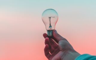 hand holding lightbulb in front of blue faded to pink background