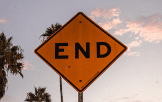 Yellow end sign with palm trees and clouds in the background